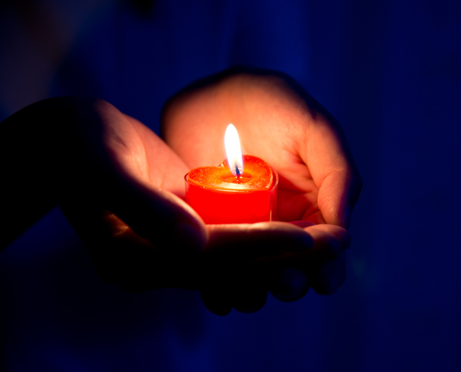 Woman hands holding burning heart-shaped candle. Symbol of hope, peace and love.